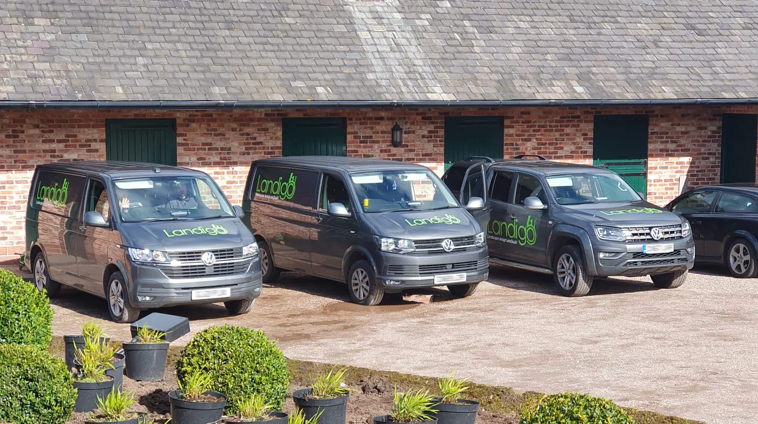 Three Landigo-branded vehicles parked outside a barn with potted plants in the foreground.