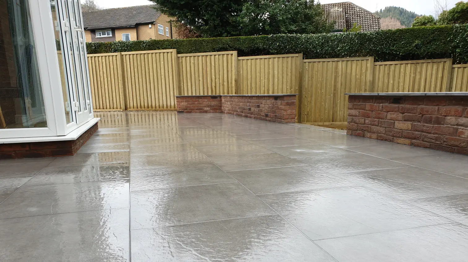A sleek, modern patio featuring grey tiles and wooden fencing.