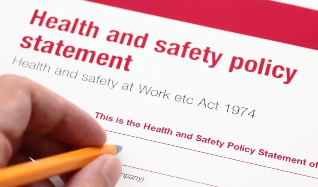 A close-up of a hand holding a pen over a health and safety policy statement document.