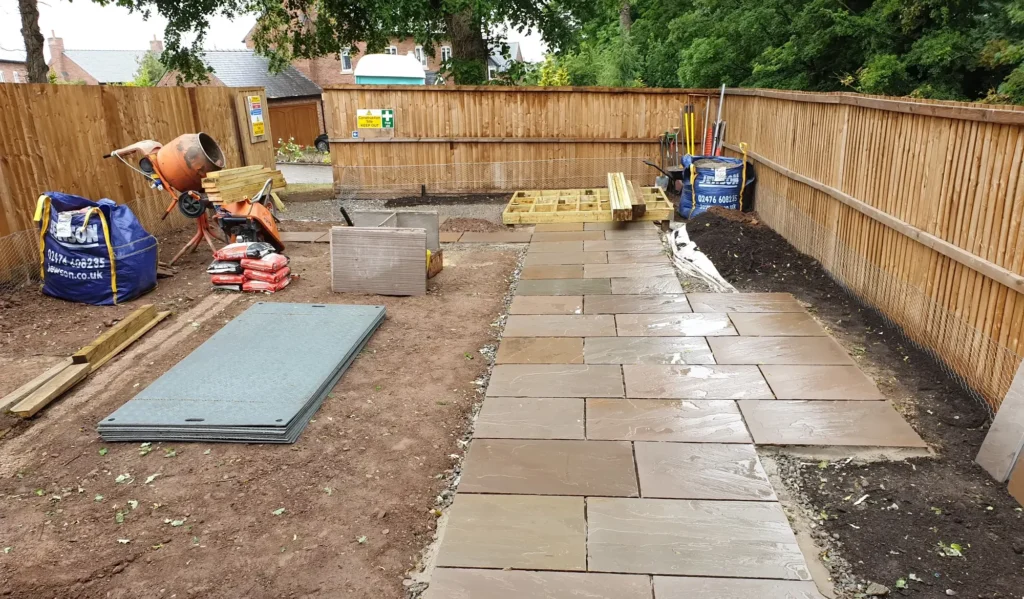 A construction site featuring a cement mixer, paving stones, and various building materials.