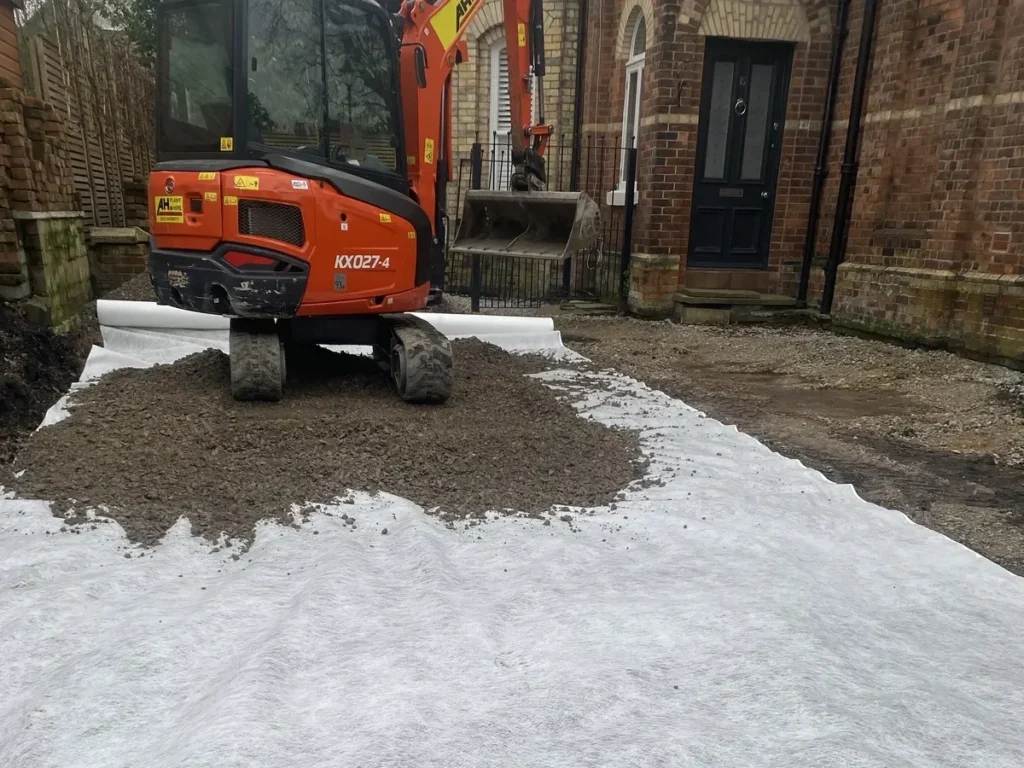 Excavator spreading subbase over geotextile membrane during Altrincham garden landscaping
