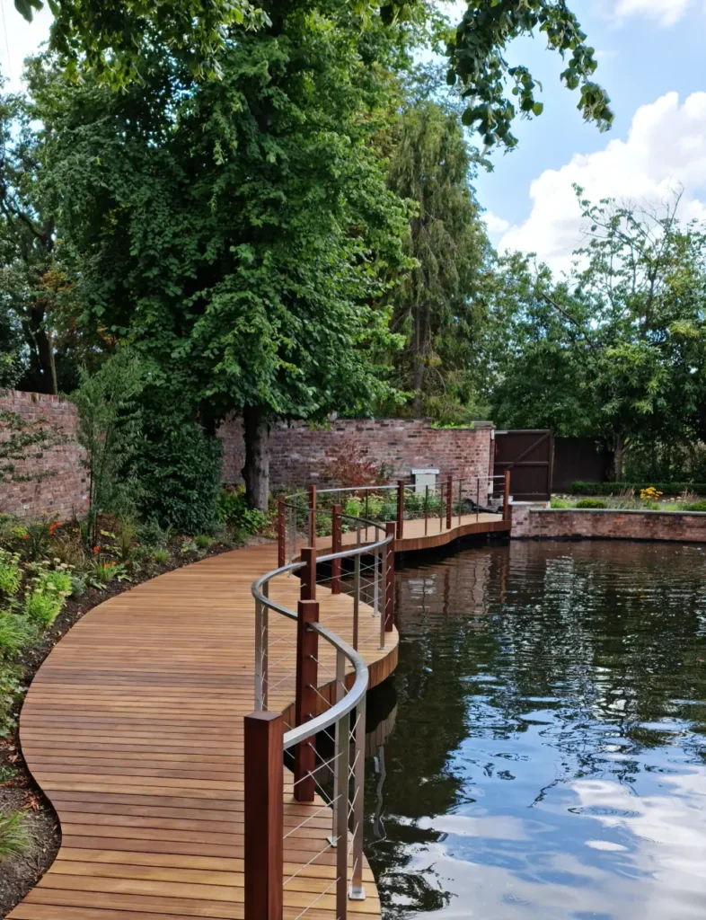Curved timber walkway around restored garden pool with brick wall and planting in Wilmslow