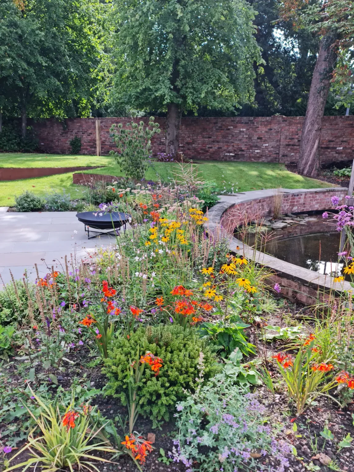 Restored pool and deck walkway surrounded by lush trees and planting in Wilmslow garden