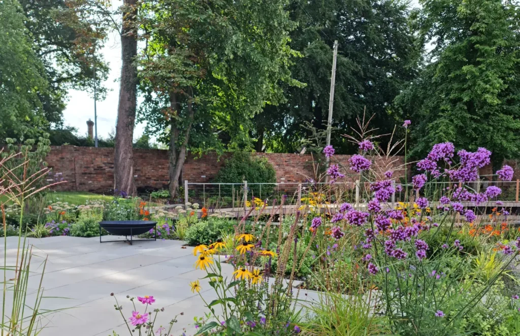 Paved lounge terrace with colourful perennials beside renovated pool in Wilmslow garden