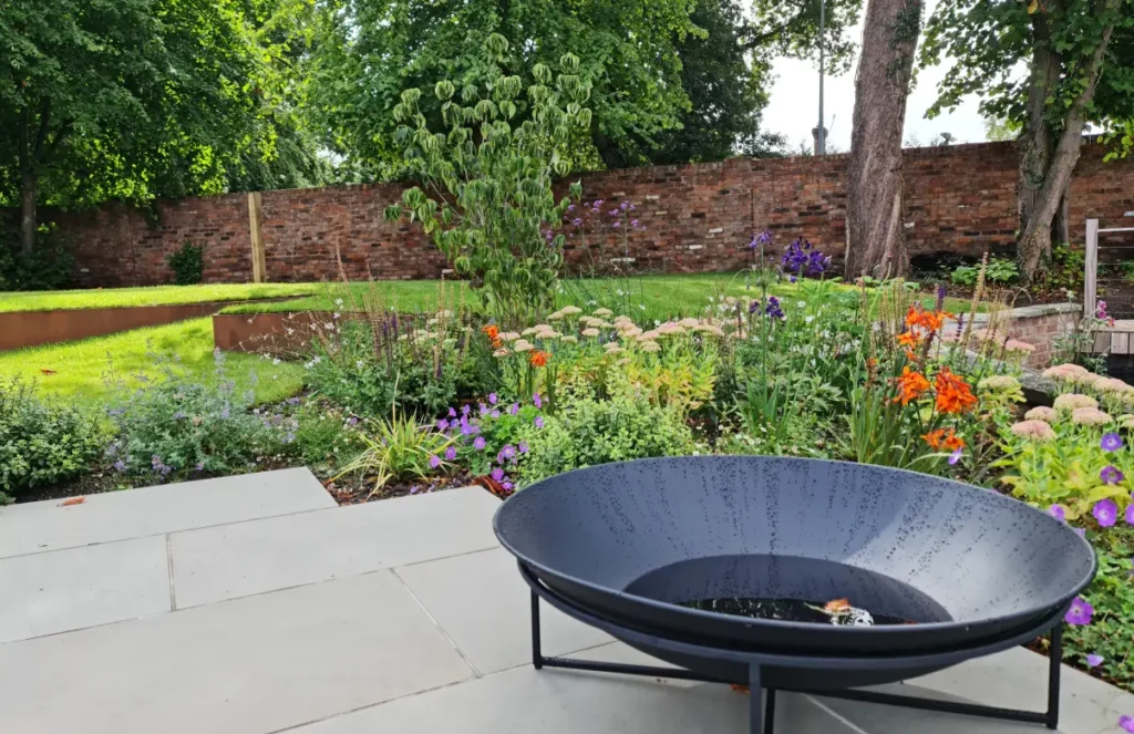 Black fire bowl on paved terrace with soft planting in Wilmslow waterside garden
