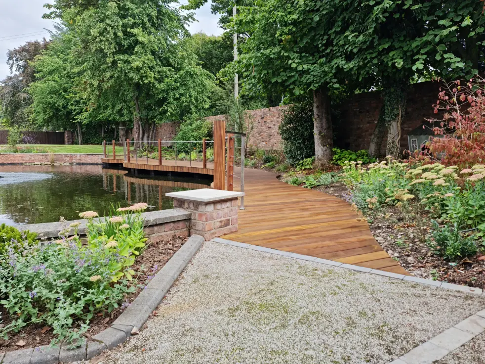 Timber deck path, gravel surface and waterside planting beside a restored garden pool