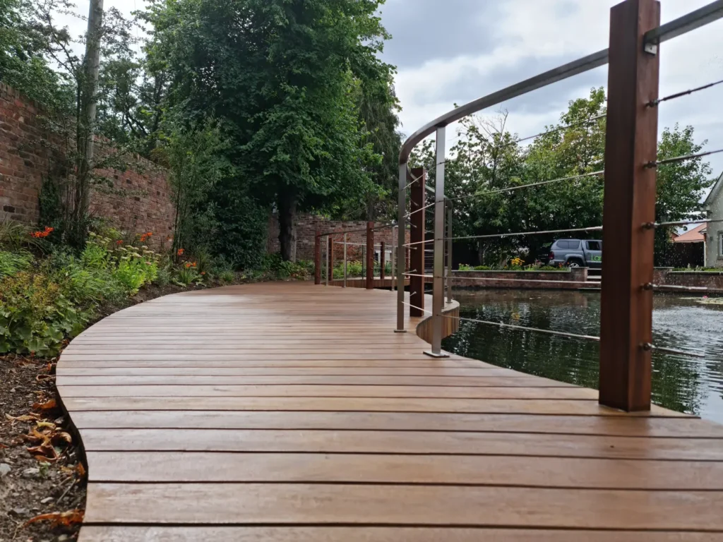 Close-up of curved yellow balau deck walkway with stainless steel railings beside restored pool