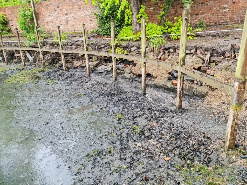 Eroding pool bank and unsafe timber deck before Wilmslow garden renovation