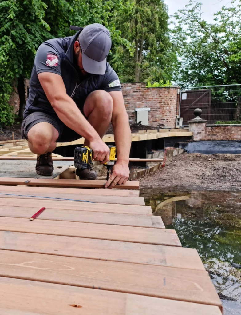 A Landigo worker focusing on building a wooden deck by a pond.
