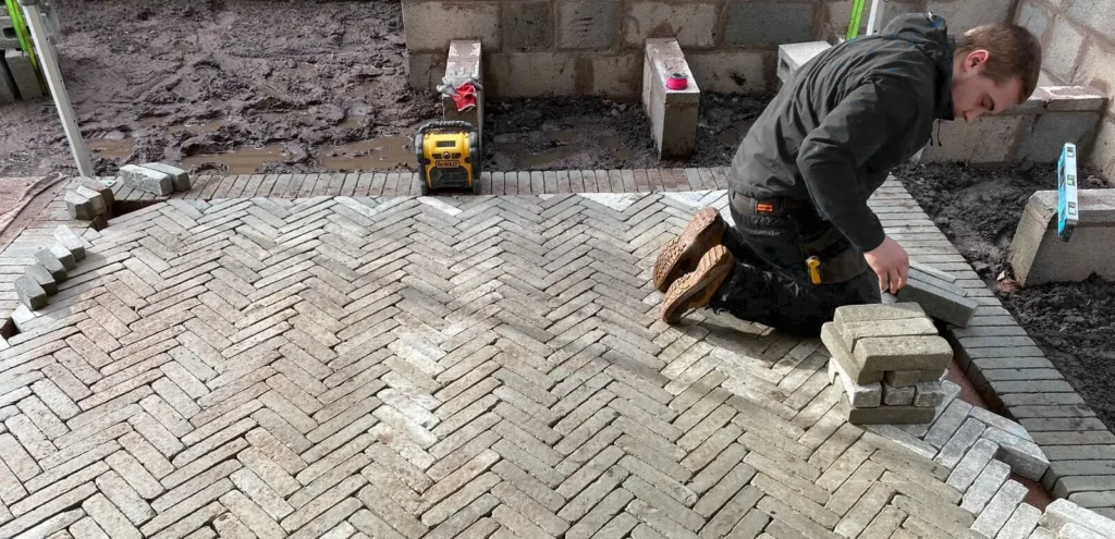 A Landigo worker laying bricks in a herringbone pattern on a construction site.