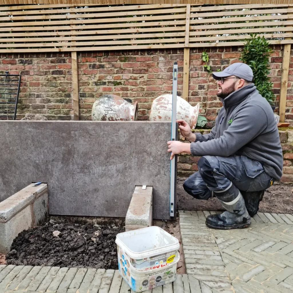 A Landigo landscaper measuring and leveling a stone structure in a garden setting.