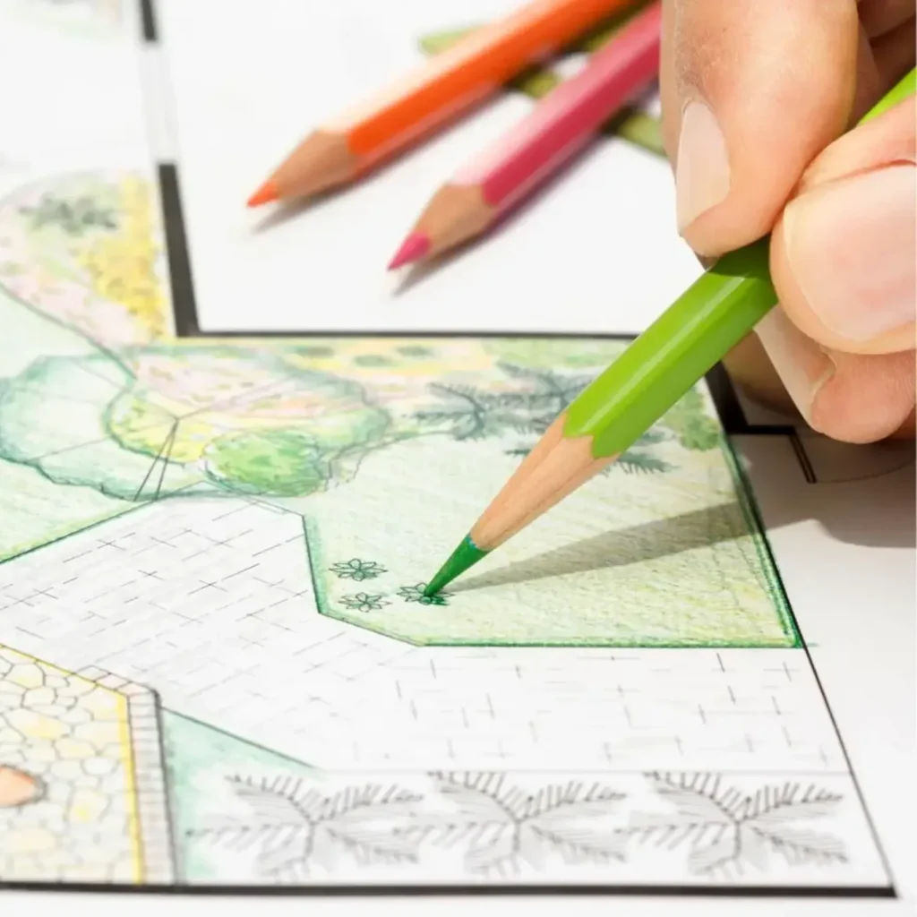 Hand holding a green pencil, adding details to a garden design sketch.