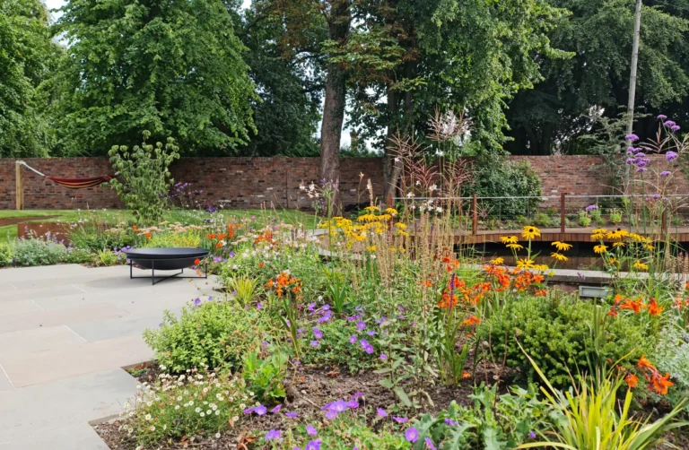 Waterside garden in Wilmslow with colourful planting and paved lounge area beside restored pool