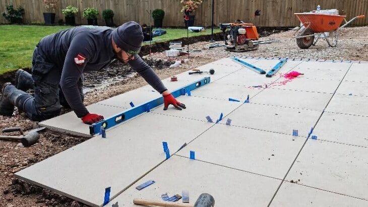 A worker laying patio slabs with a spirit level in a garden.