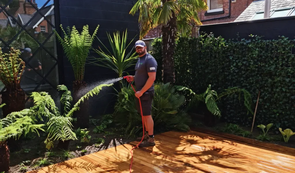 Landigo team tending to garden plants with a hose under bright sunlight.