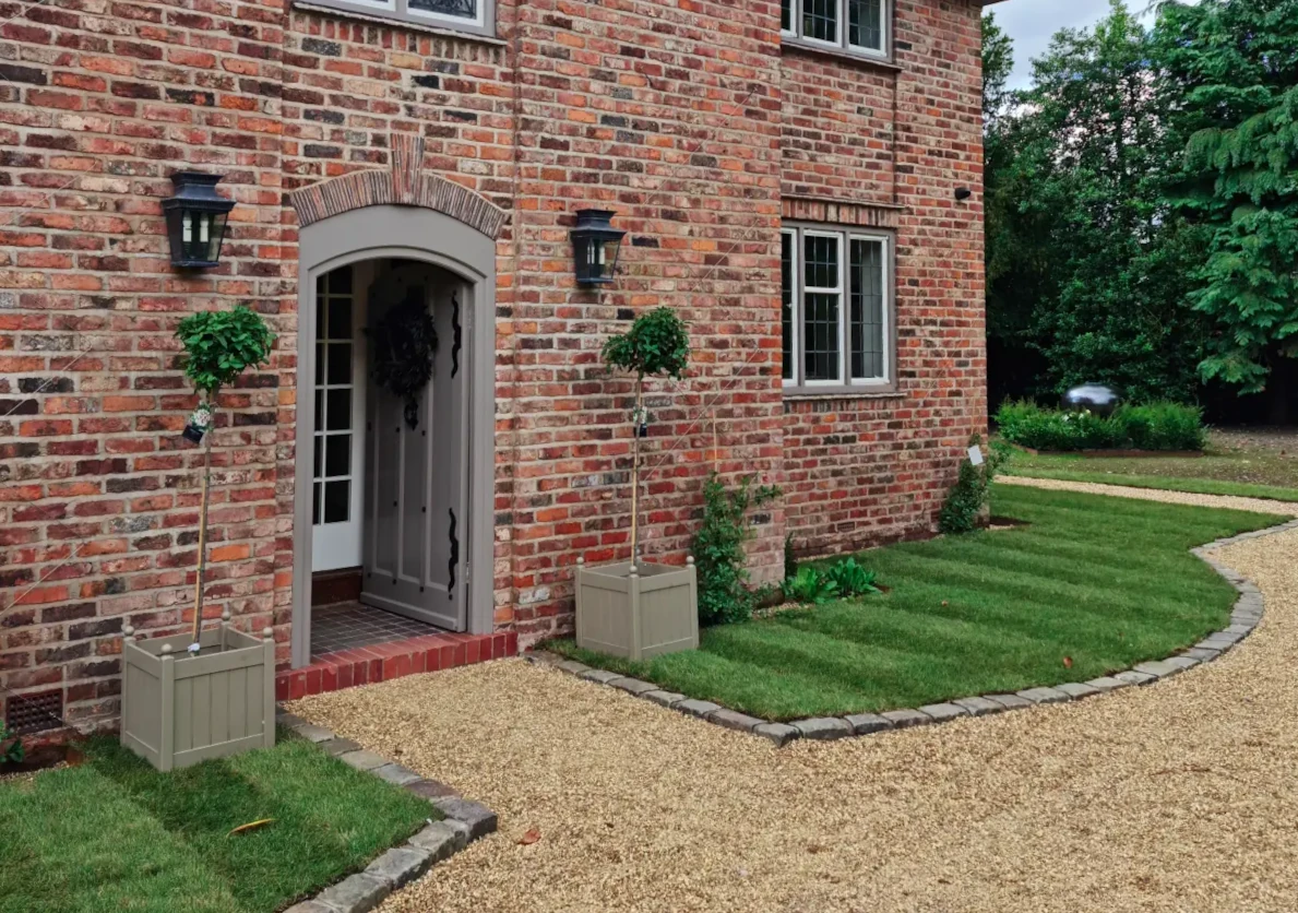 A charming brick house entrance with decorative plants and a neatly maintained garden.