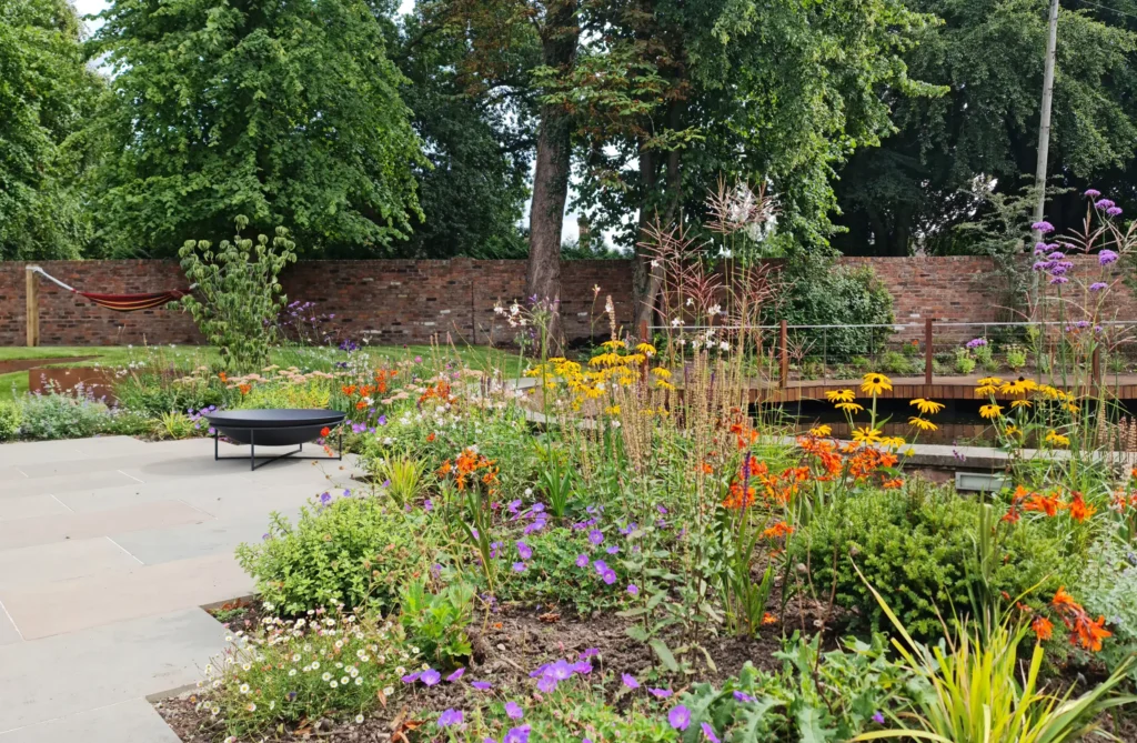 Waterside garden in Wilmslow with colourful planting and paved lounge area beside restored pool